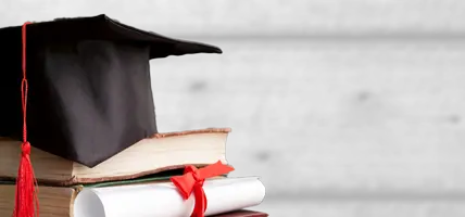 A graduation cap and diploma sit on a stack of books